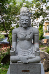 Obraz premium A stone statue of a meditating figure, possibly a deity or historical person, sits serenely in a lush garden in Po Nagar Temple, Nha Trang, Vietnam. 