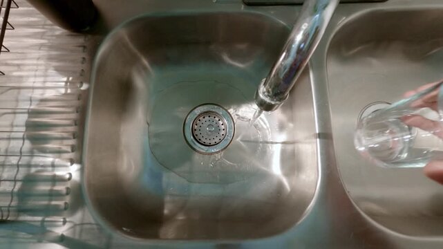 Person conserving water by filling a glass from a kitchen faucet