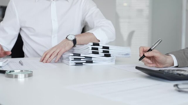Professionals handling a large stack of documents and paperwork, signing a contract in a busy office. Audit and taxes in business