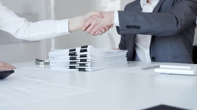 Business people shaking hands, concluding a partnership agreement after discussing documents and results. Audit and taxes in business