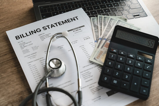 Calculator and stethoscope on billing statement with cash beside laptop performing financial calculation for medical expense accounting, billing report analysis and healthcare payment management proce