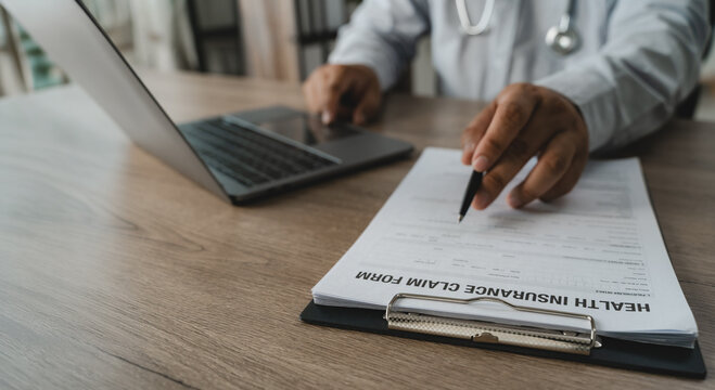 Hand holding pen reviewing health insurance claim document beside laptop and stethoscope performing document verification for medical expense accounting, compliance audit review and report management 