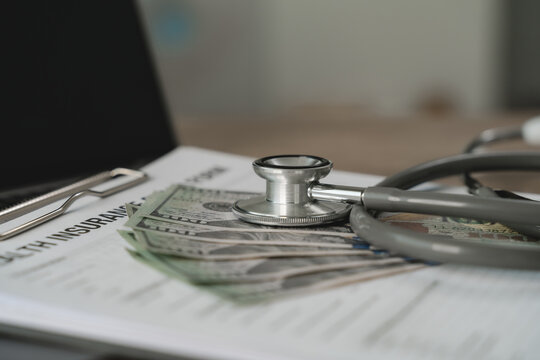 Stethoscope placed on cash over health insurance document representing financial calculation for medical expense accounting, billing analysis report and healthcare payment management process