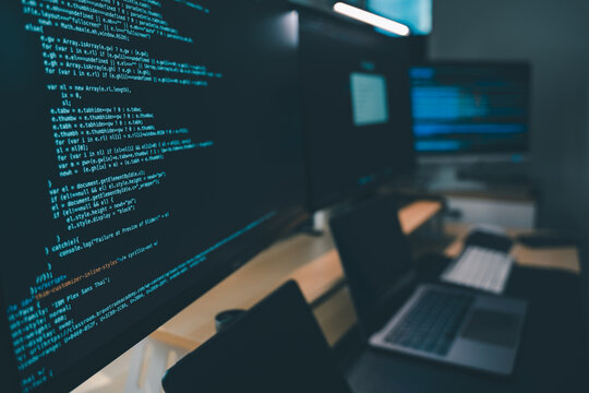 Close up of computer monitors displaying source code in a modern workstation with laptop and digital devices, showing software development workflow, programming process, and technical productivity in 