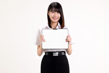 Fototapeta premium Smiling young Asian woman in student uniform holding digital tablet with blank white screen for mockup. Happy female university student showing tablet computer isolated on white background.