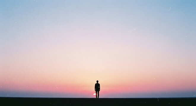 Silhouette of a person standing alone against a vast pastel sunset sky.