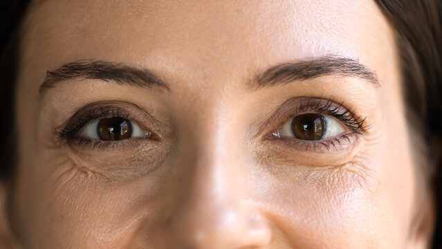 Close up cropped view of adult 30s woman upper part of face, her brown eyes looking directly at camera, watching at you, promoting eyesight checkup, sight correction, lenses for clear vision