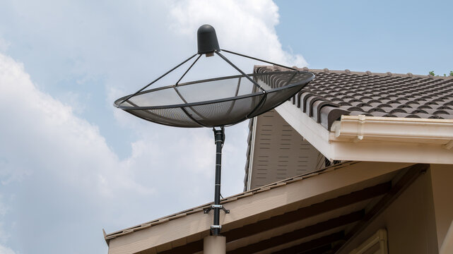 mesh satellite dish mounted on house roof under bright sky, angled for signal reception, residential installation shows communication technology integrated with tiled roofing and exterior structure