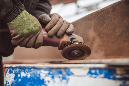 A construction worker cleans a rusty metal surface with an angle grinder. High quality photo