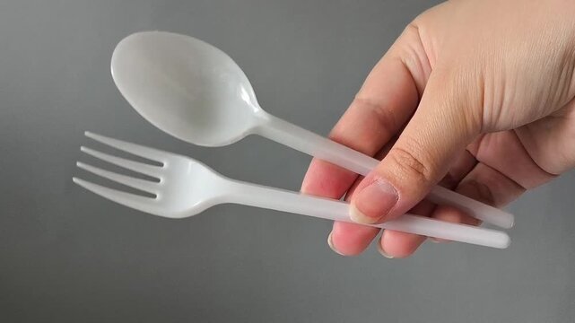 Plastic spoon and fork in hand on a gray background. set disposable takeaway tableware