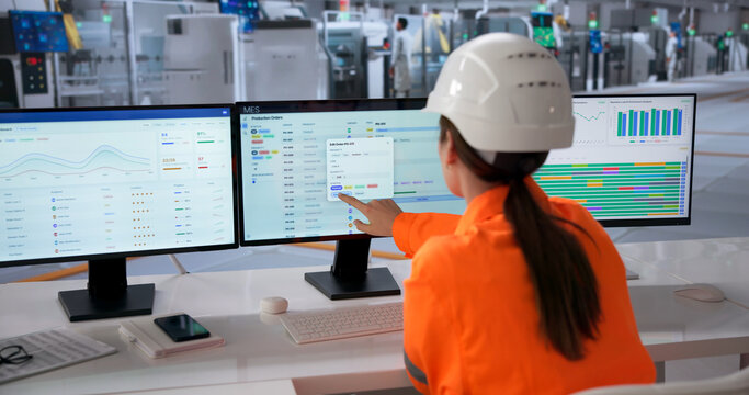 Woman Monitors Production Schedules On Multiple Screens