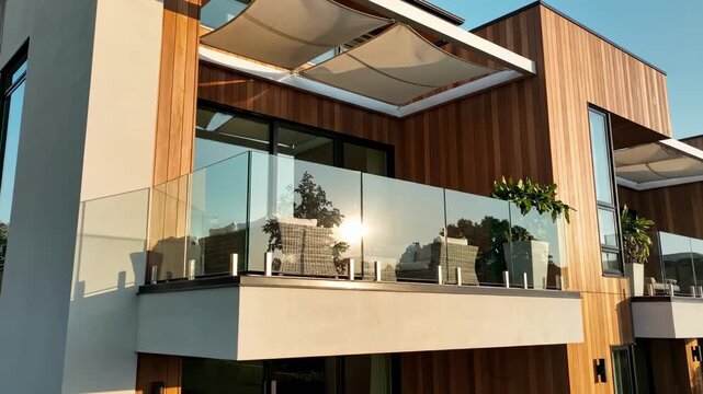 Sunlit Modern Balcony With Glass Railing And Potted Plants, Warm Wood Cladding, Retractable Awning, Reflective Windows Catching Golden Hour, Serene Outdoor Living Scene Ideal For Lifestyle.
