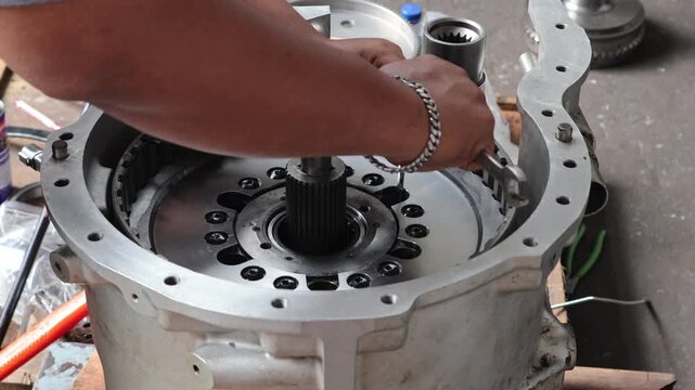 ​Close up of a technician using a hex key to tighten bolts on a metal hub inside an automatic transmission housing during a professional repair.