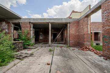 Fototapeta premium Unfinished brick building with concrete slabs, wooden beams, scattered bricks, overgrown vegetation, open doorways, abandoned construction site, cracks in concrete, wild plants spreading.