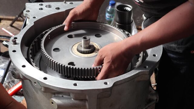 Close up of a technician's hands carefully assembling a large metal gear hub into an automatic transmission case during a mechanical overhaul.