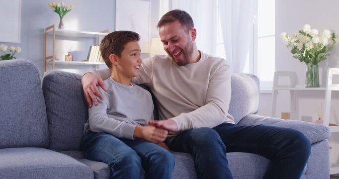 Cheerful father and son enjoying leisure time playing rock paper scissors at home. Fun and engaging game that strengthens family bonds and brings laughter through simple entertainment.