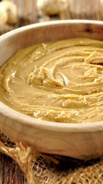 creamy peanut butter in wooden bowl on rustic background, organic vegan nut spread for healthy breakfast
