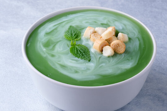 Close up of a bowl of mint or nettle leaves green soup sits on a blue background. The soup is swirled with cream, topped croutons. top view. Healthy food