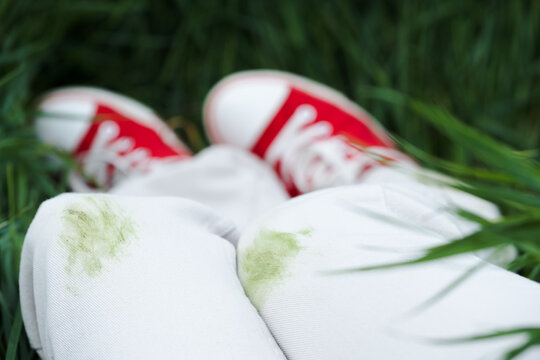 Close up of dirty stains on green grass during summer activities in the park outdoors. The individual is wearing red shoes and is outside near trees. Concept of daily stains on clothes. 