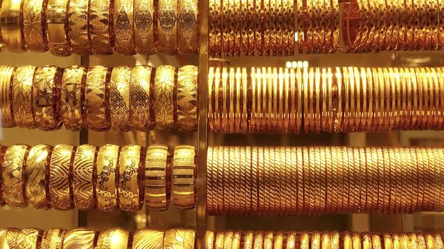 Rows of ornate gold bangles and bracelets shimmer on display rods in a jewelry shop as the camera slowly reveals the collection