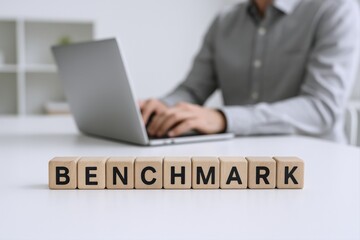 Obraz premium Wooden blocks spelling BENCHMARK with person working on laptop in blurred office background