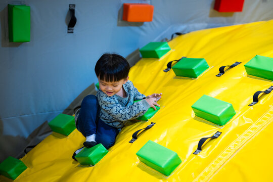 Asian boy climbing colorful inflatable slide at indoor playground, active childhood lifestyle, physical development, playful authentic moment, tactile sensory experience, vibrant indoor activity