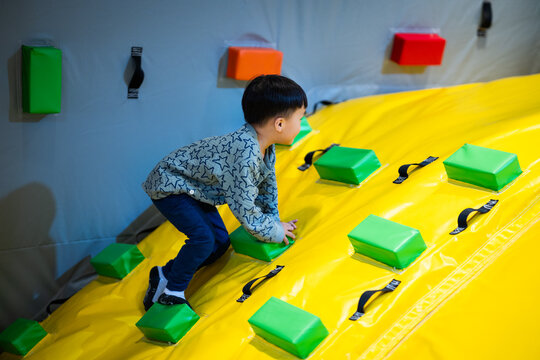 Asian boy climbing colorful inflatable slide at indoor playground, active childhood lifestyle, physical development, playful authentic moment, tactile sensory experience, vibrant indoor activity