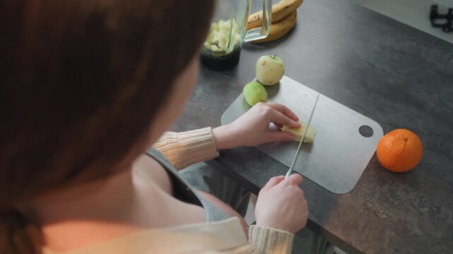 Expectant mother chopping pear by orange, prenatal meal prep scene with gentle knife work, home countertop, focus on hand movement and portioning, bright daylight, nourishing snack idea for pregnancy