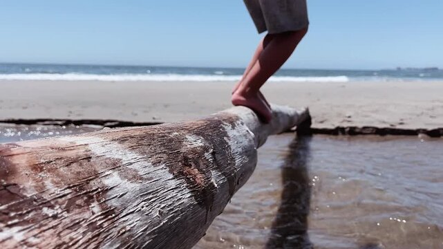 Child balancing on driftwood log at beach then jumping off, playful summer activity by ocean, outdoor seaside scene, barefoot kid exploring nature, coastal lifestyle, movement and balance concept