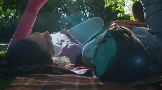 Woman and man reclining on blanket raising phone, activating holographic globe for technology demo