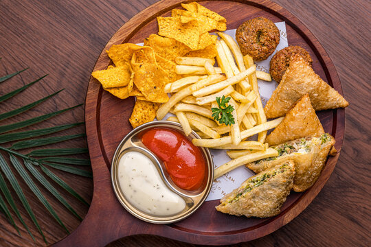 A mixed platter featuring spice-rich mutabbaq, samosas, and falafel, accompanied by crispy French fries and tortilla chips. Served warm with a choice of two sauces.