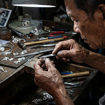 Older artisan crafting silver jewelry at a wooden workbench