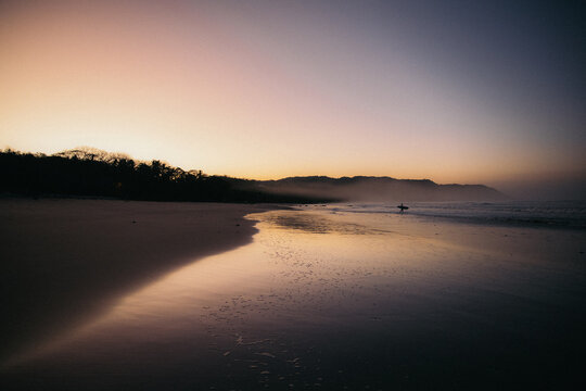 a surfer boy walking to the ocean at sunrise