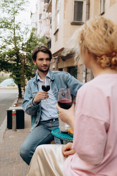 Young Man Holding Glass of Red Wine While Talking to Woman