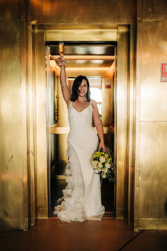 Bride toasts champagne in golden elevator with bouquet entrance