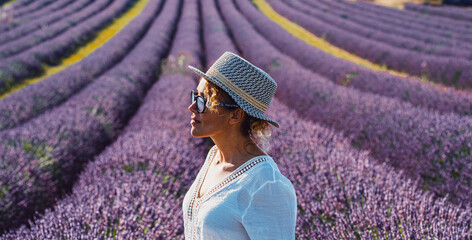 Woman wearing a straw hat and sunglasses stands thoughtfully amidst rows of blooming lavender, experiencing a serene and aromatic moment during vacation in the south of france © simona