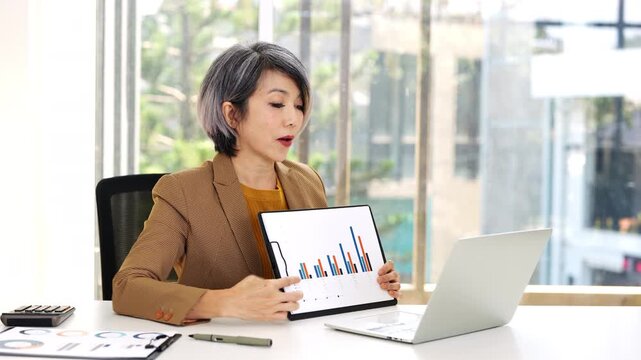 A professional woman in suits converses actively during a video call in a modern office setting, demonstrating engagement and communication.