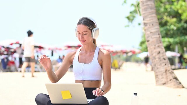 Female digital nomad works on laptop at beach, then closes it with calm relaxed gesture after exercise..