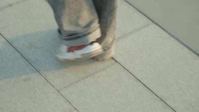 Urban casual walk. Footsteps echo along paved campus pathway. Relaxed strides beneath evening light across urban setting. Leisurely pace as sneakers glide over tiled plaza during sunset hour