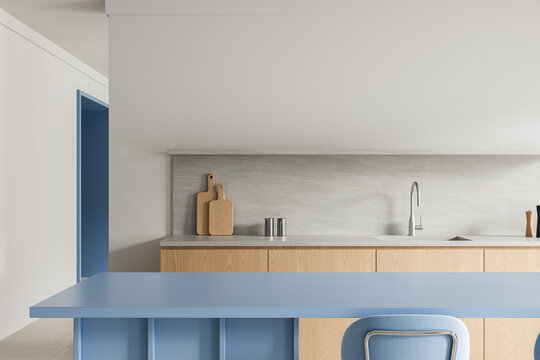 Modern minimalist kitchen interior with blue island, light wood cabinetry, soft grey backsplash and clean architectural lines. 3D Rendering