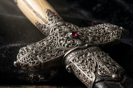 Close up of ancient silver sword hilt with intricate carvings and red gemstone