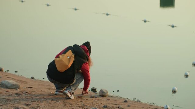 Surveyor on coast thoughtfully inspects collected river stones close to exception sources. Quiet beach wanderer meticulously analyzes small rounded rocks along shoreline during calm morning hours