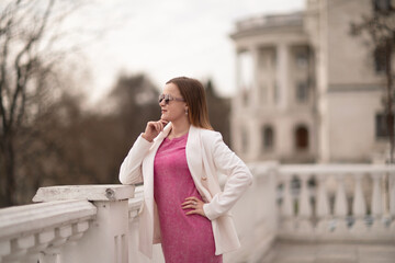 Fototapeta premium Woman PinkDress Balcony: Gazing, city balcony backdrop, spring day, thinking.