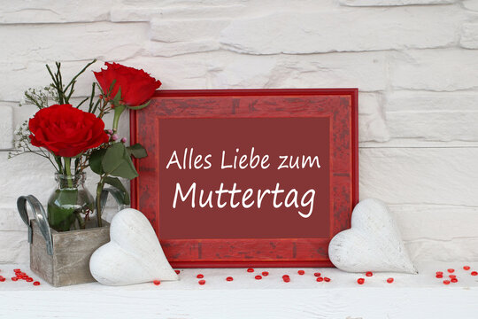 Fotorahmen mit der Beschriftung  Alles Liebe zum Muttertag. Rote Rosen und wei&szlig;e Herzen vor wei&szlig;er Steinwand,