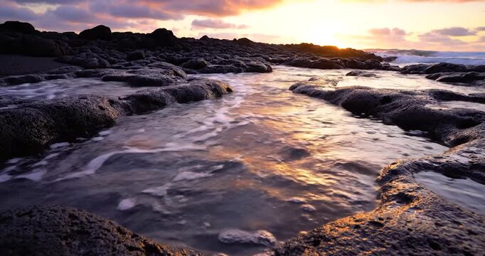 Golden sunset light reflecting on coastal tide pools with ocean waves