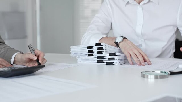 Professionals handling a large stack of documents and paperwork, signing a contract in a busy office. Audit and taxes in business