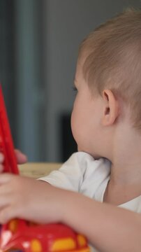 A young boy is playing with a colorful toy. The boy is focused on manipulating the toy, using red and yellow parts to engage in imaginative play.