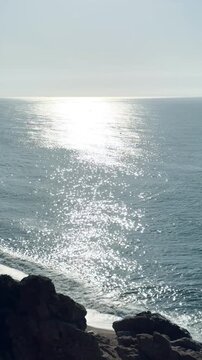 Vertical Glittering Ocean Surface with Sun Reflection and Rocky Coast, Cinematic Sea Nature Video
