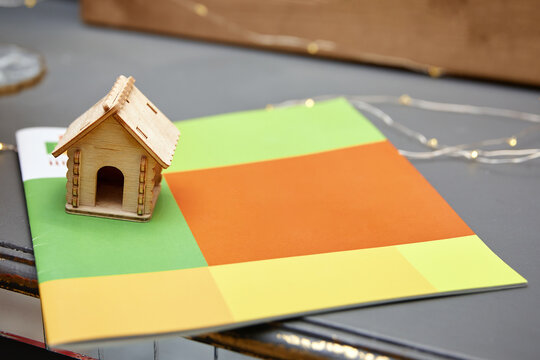 Wooden house model on a colorful brochure. Concept for real estate, mortgage, insurance, and home planning. Shallow depth of field, fairy lights background, architectural miniature.