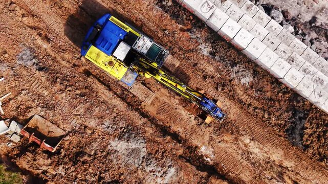 Heavy excavator standing on brown soil next to a row of concrete blocks on a construction site. Close up aerial view of excavator on construction site.